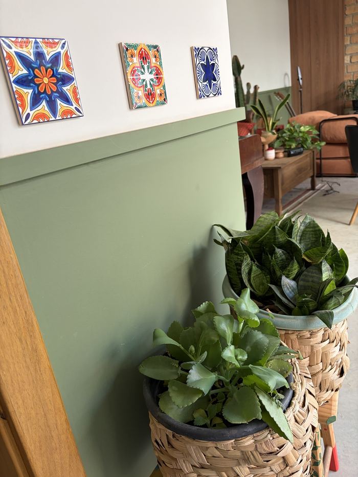 Azulejos coloridos sobre parede verde, com vasos de plantas.