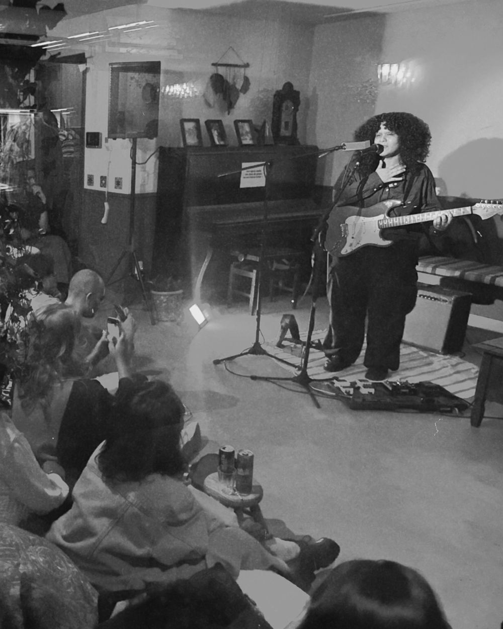 Show intimista numa sala: a artista canta com guitarra e o público assiste sentado no chão, a poucos passos dela.