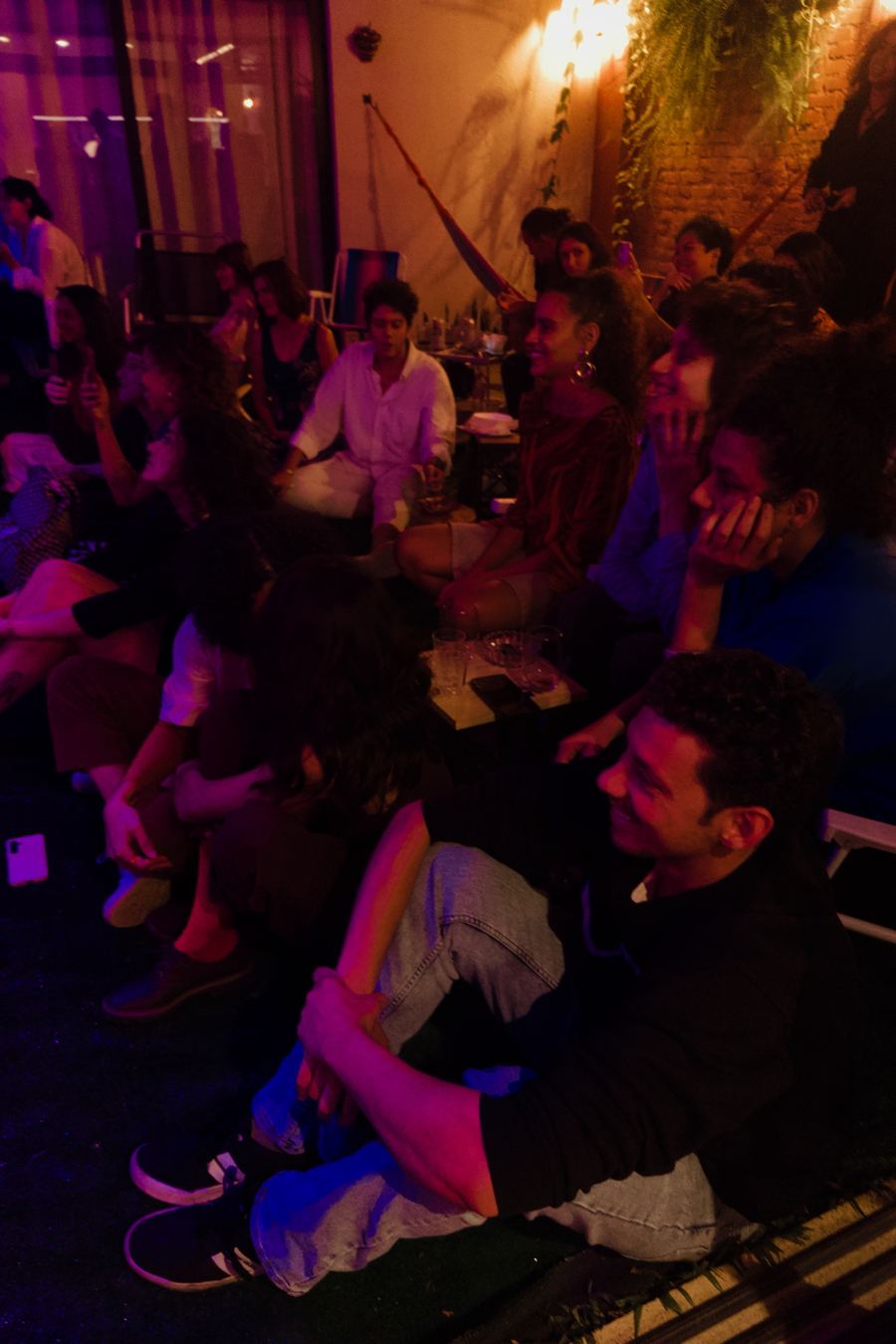 Público sentado no chão, bem perto, assistindo a um show à noite com luz quente.